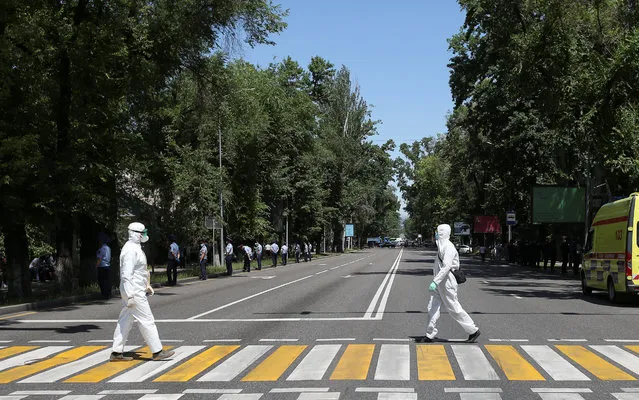 Specialists wearing protective gear, used as a preventive measure against the coronavirus disease (COVID-19), cross a road as law enforcement officers stand guard during an unsanctioned rally held by Kazakh opposition supporters in Almaty, Kazakhstan on June 6, 2020. (Photo by Pavel Mikheyev/Reuters)
