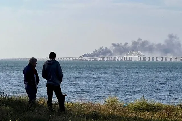 People look at thick black smoke rising from a fire on the Kerch bridge that links Crimea to Russia, after a truck exploded, near Kerch, on October 8, 2022. (Photo by AFP Photo/Stringer)