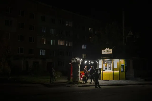 People stand outside a bar in Borodyanka, Kyiv region, Ukraine, Friday, October 21, 2022. Russia has declared its intention to increase its targeting of Ukraine's power, water and other vital infrastructure in its latest phase of the nearly 8-month-old war. Ukrainian President Volodymyr Zelenskyy says that Moscow's forces have destroyed nearly a third of the country's power stations since Oct. 10. (Photo by Emilio Morenatti/AP Photo)
