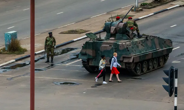 Young women walk past an armoured personnel carrier that stations by an intersection as Zimbabwean soldiers regulate traffic in Harare on November 15, 2017. Zimbabwe' s military appeared to be in control of the country on November 15 as generals denied staging a coup but used state television to vow to target “criminals” close to President Mugabe. (Photo by Jekesai Njikizana/AFP Photo)