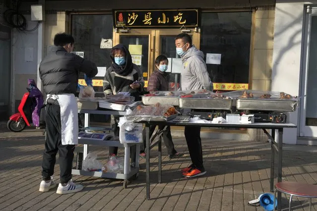Residents buy cooked food from a vendor selling on the street after restaurants were order closed in Beijing, Friday, November 25, 2022. (Photo by Ng Han Guan/AP Photo)