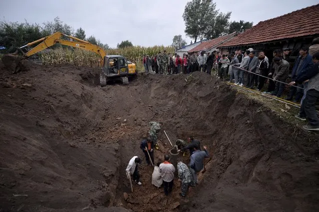 People watch rescuers try to pull 50-year-old woman Zhao Hongxia out of a well in Xinhu township of Changchun, Jilin province, China, September 24, 2015. Zhao, who suffered from mental illness, was killed after falling into and being stuck in the well at a depth of 13 metres for over five hours. The well was very narrow so rescuers had to excavate a wider opening and dismantle the well piece by piece to reach her, local media reported. (Photo by Reuters/Stringer)