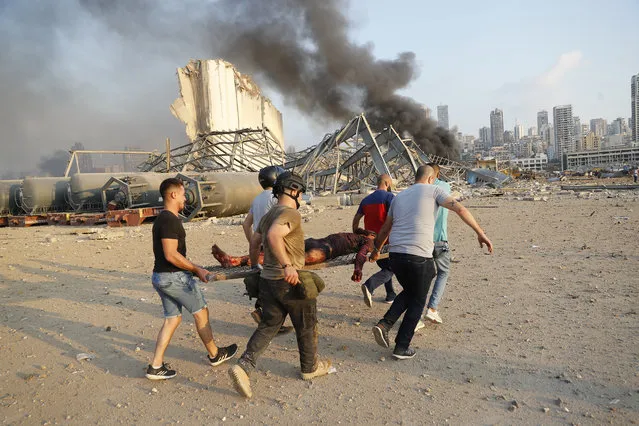 Civilians carry a victim at the explosion scene that hit the seaport, in Beirut Lebanon, Tuesday, August 4, 2020. (Photo by Hussein Malla/AP Photo)