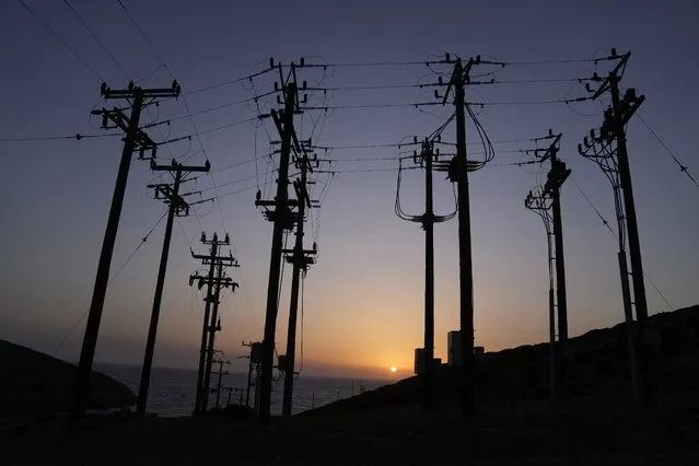 The sun sets behind electricity posts on the Aegean Sea island of Tilos, southeastern Greece, Monday, May 9, 2022. When deciding where to test green tech, Greek policymakers picked the remotest point on the map, tiny Tilos. Providing electricity and basic services, and even access by ferry is all a challenge for this island of just 500 year-round inhabitants. It's latest mission: Dealing with plastic. (Photo by Thanassis Stavrakis/AP Photo)