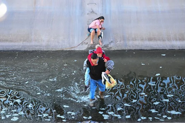 A family of migrants from Columbia makes their way through a water canal after crossing under a hole in the US-Mexico border wall in El Paso, Texas, on December 19, 2022. The US Supreme Court halted Monday the imminent removal of a key policy used since the administration of president Donald Trump to block migrants at the southwest border, amid worries over a surge in undocumented immigrants. An order signed by Chief Justice John Roberts placed a stay on the removal planned for Wednesday of Title 42, which allowed the government to use Covid-19 safety protocols to summarily block the entry of millions of migrants. (Photo by Patrick T. Fallon/AFP Photo)