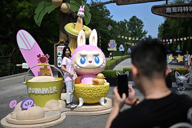 This picture taken on June 18, 2025 shows a woman posing for a picture next to the character Mokoko as she visits Pop Mart's theme park Pop Land in Beijing. (Photo by Pedro Pardo/AFP Photo)
