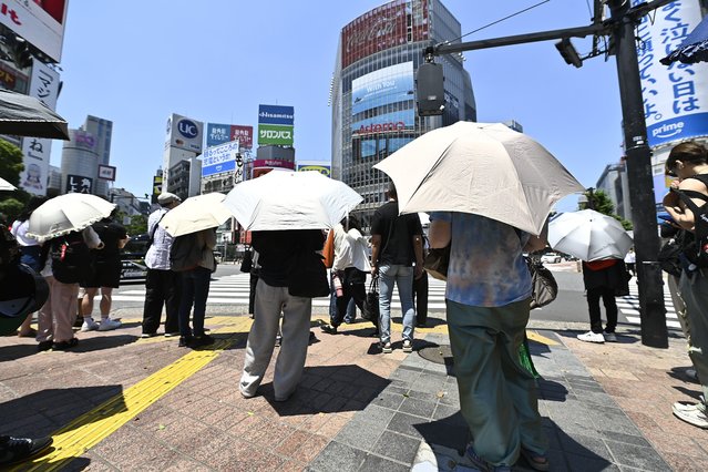 People wait at the iconic Shibuya crossroad shield themselves with a parasol on June 17, 2025, in Tokyo, Japan, as Japan's capital is sweltering under an unusually intense heatwave. With temperatures reaching 34°C today in central Tokyo, the city is nearing its all-time June heat record. This early-season extreme event is rapidly becoming one of the year's defining climate stories. (Photo by David Mareuil/Anadolu via Getty Images)