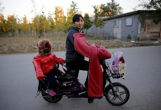 Lv Hongli and her second daughter ride on a bicycle while posing at a migrant workers' village in Beijing, China October 30, 2015. Lv Hongli, 34, a restaurant worker, said she has two children and paid the 5,000 RMB fine to the government after her second child was born. She said the rule change is too late for her but it would be good for those who want to have two children. (Photo by Kim Kyung-Hoon/Reuters)