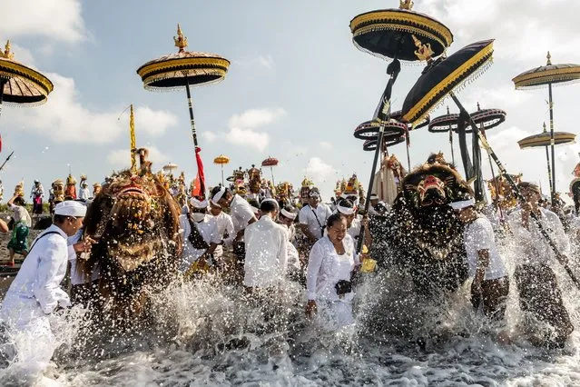 Balinese Hindus people carry sacred mask, sacred effigies and ritual paraphernalia during Melasti Ritual prior to Nyepi Day on March 19, 2023 at Siyut Beach, in Gianyar Bali, Indonesia. After three years of performing purification ceremony ahead of Nyepi Day on a small scale due to the COVID-19 pandemic Balinese Hindus dressed in predominantly white attire carried sacred effigies of gods and goddesses and ritual paraphernalia from their village temples to the beach to perform a purification ceremony called the Melasti ritual. Balinese Hindus believe the Melasti ritual is a must perform ahead of Nyepi Day, The Day of Silence, to cleanse the soul and nature, recharge the supernatural power of the temples sacred objects and cleanse the temple paraphernalia. The Nyepi Day is a national holiday in Indonesia and is a day for self-reflection and abstaining from distractions such as entertainment. (Photo by Agung Parameswara/Getty Images)