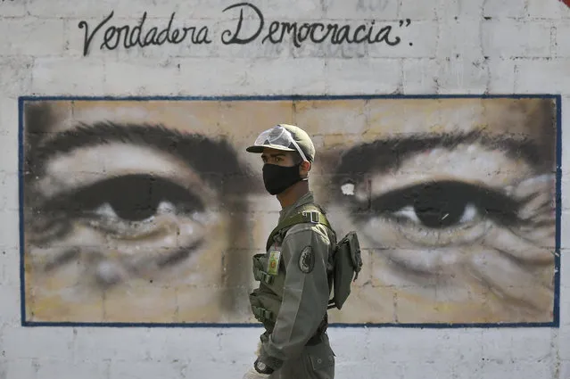 A soldier guards a voting poll at a school that has the eyes of the late President Hugo Chavez painted on a wall during elections to choose members of the National Assembly in Caracas, Venezuela, Sunday, December 6, 2020. The vote, championed by President Nicolas Maduro, is rejected as fraud by the nation's most influential opposition politicians. (Photo by Matias Delacroix/AP Photo)