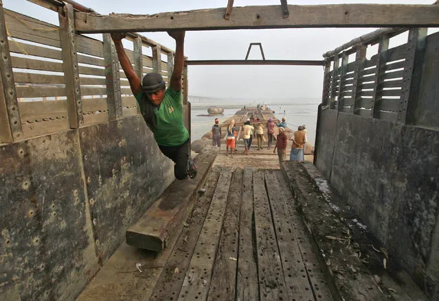 A labourer uses his feet to unload a wooden log which is used to construct a temporary bridge made up for the Magh Mela festival on the river Ganges in Allahabad, India, December 11, 2015. The festival is an annual religious event held during the Hindu month of Magh, when thousands of Hindu devotees take a holy dip in the waters of the Ganges. (Photo by Jitendra Prakash/Reuters)