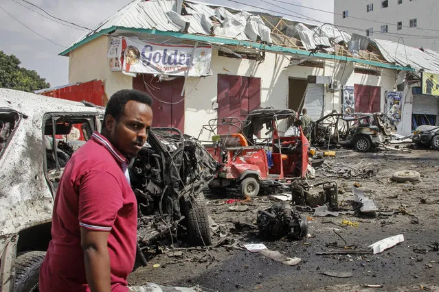 A man walks past wreckage at the scene of a bombing in Mogadishu, Somalia, Saturday, February 13, 2021. Police say a suicide bomber died and a number of civilians were wounded when a vehicle exploded near a checkpoint outside the presidential palace in Somalia's capital, Mogadishu. (Photo by Farah Abdi Warsameh/AP Photo)