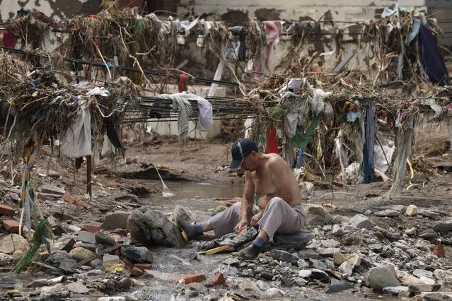 A man washes his clothes in a stream near debris left over after flood waters devastated the village of Nanxinfang on the outskirts of Beijing, Friday, August 4, 2023. (Photo by Ng Han Guan/AP Photo)