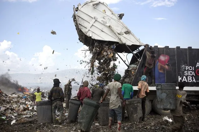 In this August 23, 2018 photo, Changlair Aristide, in red shirt at center, waits for a truck to finish dumping its load at the Truitier landfill in the Cite Soleil slum of Port-au-Prince, Haiti. Both men and women sift through the smelly debris in search of anything useful to use or sell, and violence sometimes breaks out as collectors fight for the most valuable hauls. (Photo by Dieu Nalio Chery/AP Photo)