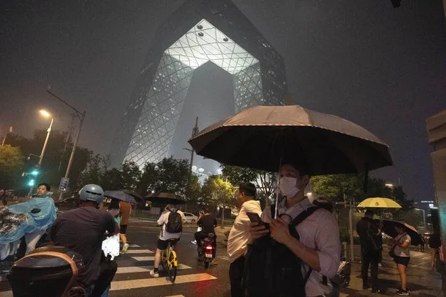 Residents use umbrellas as it starts to rain near the iconic CCTV tower in Beijing, Friday, August 11, 2023. (Photo by Ng Han Guan/AP Photo)