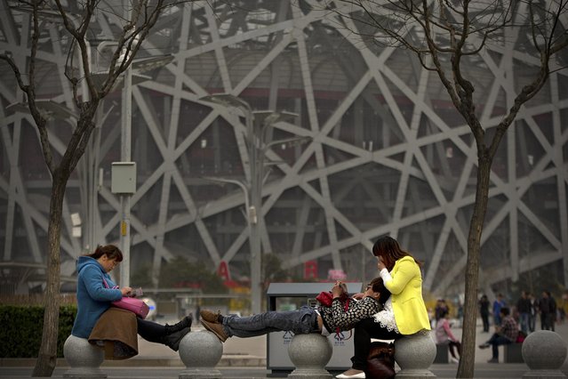 Visitor stretch out along pillars near the Beijing National Stadium, also known as the Birds Nest, in Beijing, Sunday, March 29, 2015. Organizers of the IAAF World Championships officially announced the start of ticket sales for the track and field contest on Sunday, which will be held at the stadium from August 22 to 30. (Photo by Mark Schiefelbein/AP Photo)