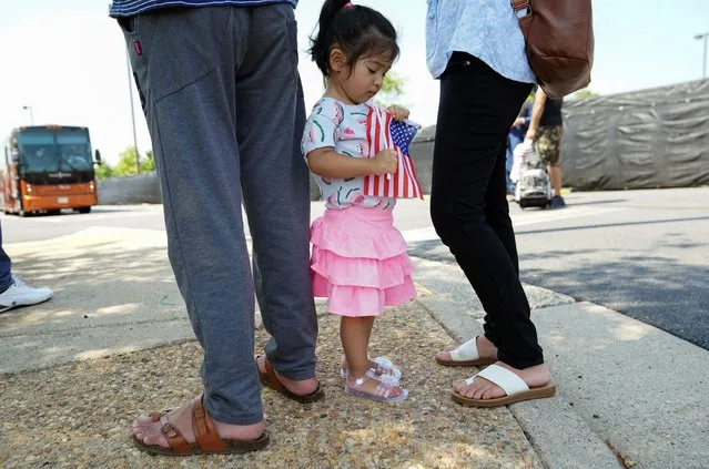 A girl holding a U.S. flag waits with her parents for Afghan relatives at a processing center for refugees evacuated from Afghanistan at the Dulles Expo Center near Dulles International Airport in Chantilly, Virginia, U.S., August 24, 2021. (Photo by Kevin Lamarque/Reuters)