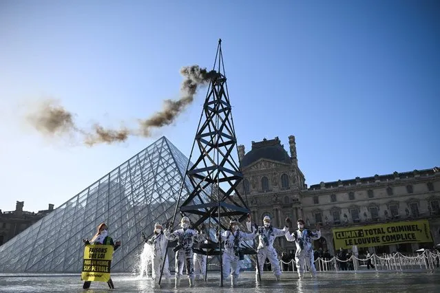 Greenpeace activists wearing the uniform of petroleum workers stand beside a smoking “oil well tower” during an action in front of The Louvre Museum Pyramid in Paris on October 6, 2021 as they protest against French energy company Total and continued world fossil fuel production and consumption. (Photo by Anne-Christine Poujoulat/AFP Photo)