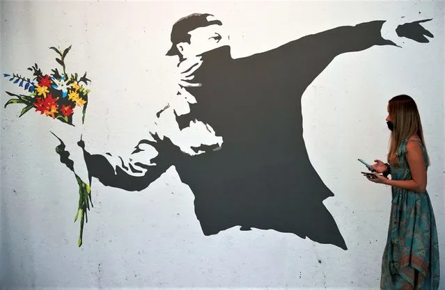 A woman walks past a reproduction of the work “Rage Flower Thrower” by British anonymous street artist Banksy, on display in the exhibition “Banksy. The Art of Protest” at the Museu del Disseny in Barcelona, Spain, 12 November 2021. The exhibition runs from 12 November 2021 to 13 March 2022. (Photo by Alejandro Garcia/EPA/EFE)