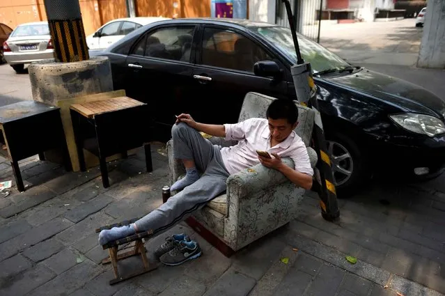 A man looks at his mobile phone while resting beside a car park in Beijing on April 30, 2015. (Photo by Greg Baker/AFP Photo)