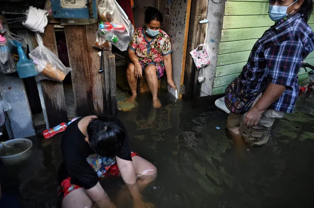 Residents sit on the doorsteps of their flooded home as water from the Chao Praya River floods low lying areas around Bang Phlat district in Bangkok on November 8, 2021. (Photo by Lillian Suwanrumpha/AFP Photo)