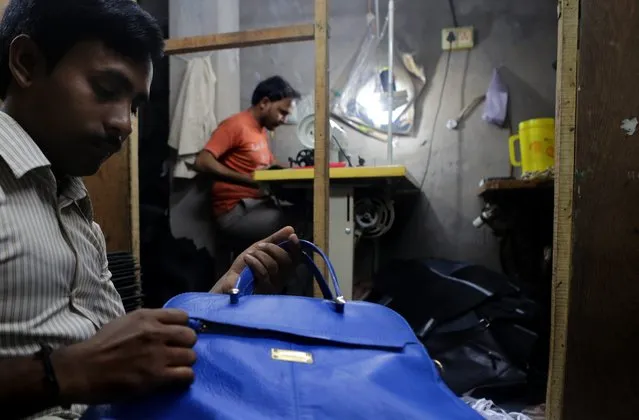 Indian bag maker Latif Muhammad (L) checks a finished leather bag while another worker is busy with stiching at a leather goods workshop at Topsia in Calcutta, eastern India, 19 November 2013. (Photo by Piyal Adhikary/EPA)