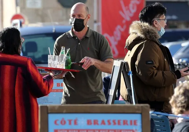 A waiter wearing a face mask at a terrace of restaurant talks to person in Saint-Jean-de-Luz southwestern France, Wednesday, February 2, 2022. England, France, Ireland, the Netherlands and several Nordic countries have taken steps to end or loosen their restrictions. Step by step, many countries are easing their COVID-19 restrictions amid hopes the omicron wave may have passed its peak. (Photo by Bob Edme/AP Photo)