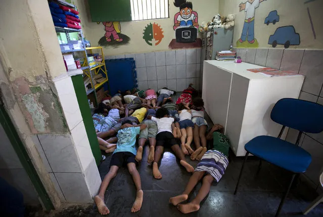 In this April 5, 2017 photo published on April 13, students practice taking cover against shootings between gangs and police, in a classroom at the Uere special needs school, in the Mare slum in Rio de Janeiro, Brazil. With rival drug dealers on practically every corner and a militarized campaign by authorities to take them out, shootouts have become so common that the school holds drills for students to practice taking cover quickly. (Photo by Silvia Izquierdo/AP Photo)
