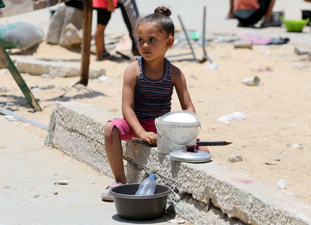 A girl sits as Palestinians gather to receive food cooked by a charity kitchen, amid shortages of aid supplies in Khan Younis, in the southern Gaza Strip, on June 19, 2024. (Photo by Hatem Khaled/Reuters)