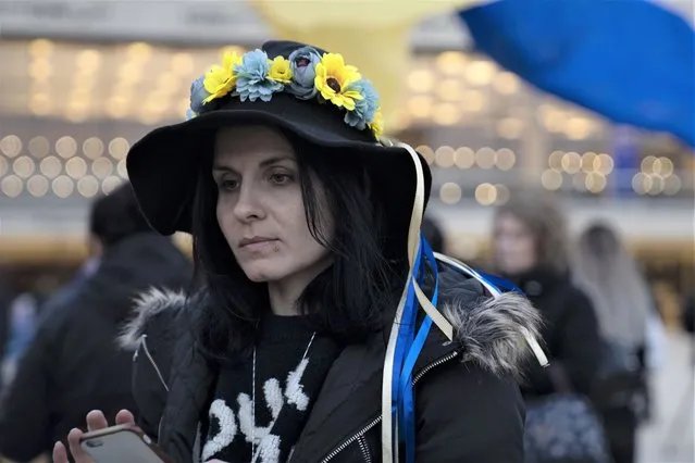 A woman wears a flower crown in the colors of the Ukranian flag in Habima Square in Tel Aviv, Israel, to watch Ukrainian President Volodymyr Zelenskyy in a video address to the Knesset, Israel's parliament, Sunday, March 20, 2022. (Photo by Maya Alleruzzo/AP Photo)