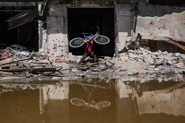 A Palestinian youth carries his bike as he walks on the rubble of destroyed buildings along the edge of a pool of stagnant water in Khan Yunis in the southern Gaza Strip on July 19, 2024, as the conflict between Israel and the Palestinian militant group Hamas continues. The Israeli health ministry said poliovirus type 2 was detected in Gaza sewage samples tested in an Israeli laboratory, adding that the World Health Organization had made similar findings. The war has destroyed much of Gaza's housing and other infrastructure, leaving almost all of the population displaced and short of food and drinking water. The Israeli health ministry said poliovirus type 2 was detected in Gaza sewage samples tested in an Israeli laboratory, adding that the World Health Organization had made similar findings. (Photo by Bashar Taleb/AFP Photo)