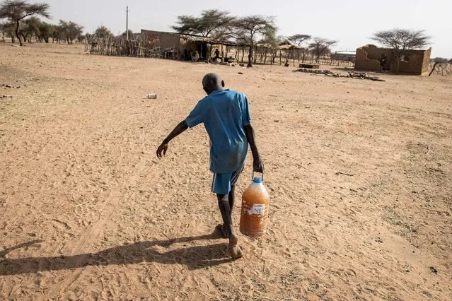 A young boy carries a bottle of drinking water back home in the village of Madina Torobe, Matam Region on March 11, 2022. Access to drinking water in the North West areas of Senegal is a constant issue. Through the months of November to August no rain will fall, rivers and natural lakes dry up. Not all areas have drinking wells and flowing taps and if there are, the water is dirty or specifically for animals. Fulani Pastoralists and families living in these remote villages sometimes need to resort to digging large holes in dried out river beds in search of cleaner drinking water from them and their animals. (Photo by John Wessels/AFP Photo)