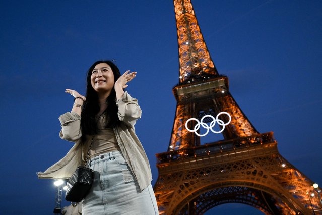 A woman poses in front of the Eiffel Tower with the Olympic rings displayed on it ahead of the Paris 2024 Olympic and Paralympic games, in Paris on July 21, 2024. (Photo by Luis Robayo/AFP Photo)