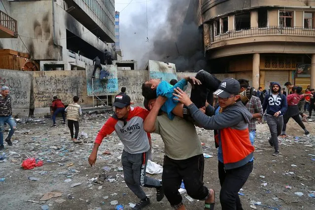 A wounded protester is carried to receive first aid during clashes with security forces on Rasheed Street in Baghdad, Iraq, Thursday, November 28, 2019. Anti-government protests have gripped Iraq since Oct. 1, when thousands took to the streets in Baghdad and the predominantly Shiite south. The largely leaderless movement is accusing the government of being hopelessly corrupt, and also decries Iran's growing influence in Iraqi state affairs. (Photo by Khalid Mohammed/AP Photo)