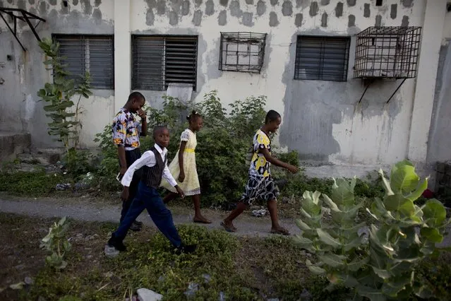 In this June 27, 2015 photo, Johnly Clif Gaspard, back left, heads to Sunday morning Mass with his mother and two younger siblings, as they leave the abandoned shipping depot where they live in Port-au-Prince, Haiti. Although his mother works full-time in a button factory and Gaspard earns money selling motorized toys built from scrap materials, the family cannot afford to move out of the depot where they are squatting along with five other families. (Photo by Rebecca Blackwell/AP Photo)