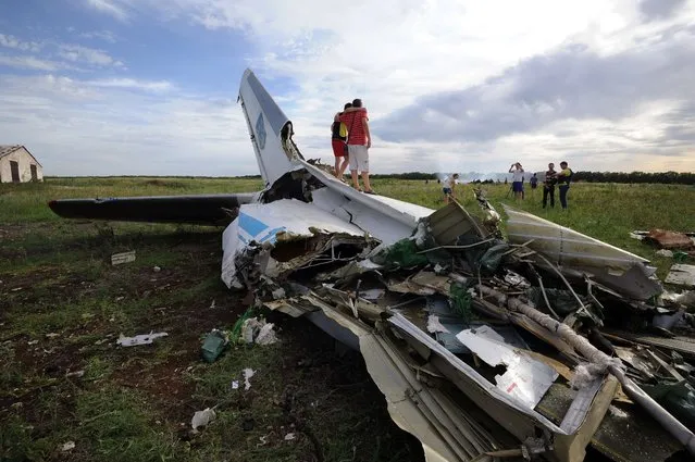 People pose on July 14, 2014 while standing on the wreckage of a Ukrainian AN-26 military transport plane after it was shot down by a missile in the village of Davydo-Mykilske, east of Lougansk near the Russian border. According to villagers of Davydo-Mykilske, many of whom rushed to the crash site on motorcycles and bikes to see if they could collect parts from the wreckage, the plane came down at around 12:30 (9:30 GMT). (Photo by Dominique Faget/AFP Photo)