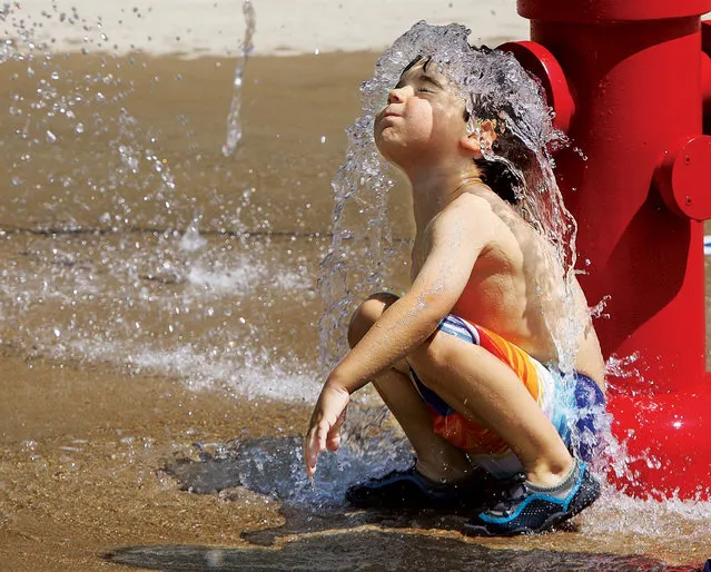 Adrian Sova, 4, squats down in front of the replica fire hydrant in the Splashpark to take the plunge on one of the last days of summer vacation in Hartford, Ill., Monday August 17, 2015. (Photo by John Badman/The Telegraph via AP Photo)