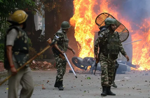 Indian security forces walk past burning vehicles set alight by rioting followers of a religious leader convicted of rape in Panchkula on August 25, 2017. (Photo by Money Sharma/AFP Photo)