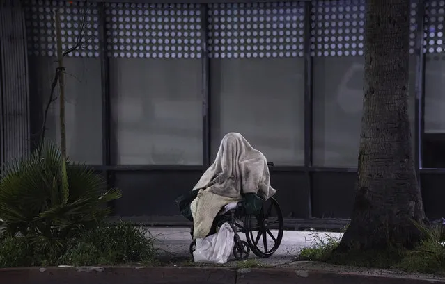 A homeless person sits on a wheelchair under rainy weather on Sunset Blvd., in the Echo Park neighborhood of Los Angeles Monday, April 6, 2020. One population is particularly vulnerable to contracting and spreading the coronavirus: the homeless. Officials have vowed repeatedly to get them indoors, but testing shortages and bureaucratic wrangling are making it difficult. Relatively few of California's 150,000 homeless population have been moved into individual quarters. It's unclear how many even have the highly contagious virus. It's a problem playing out nationwide and it's unclear how many may even have coronavirus. (pHOTO BY Damian Dovarganes/AP Photo)