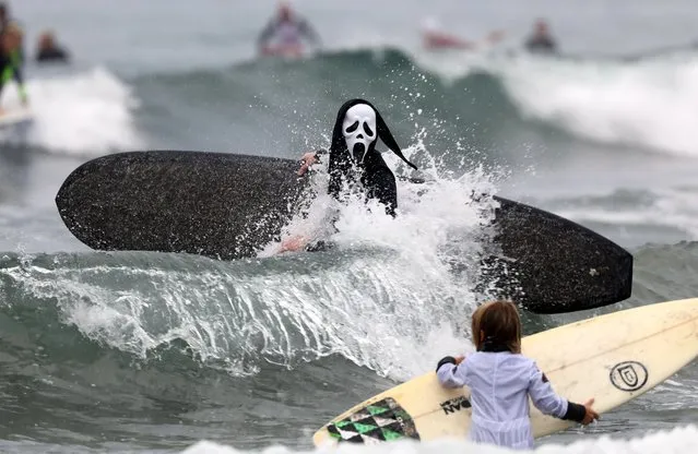 A surfer dressed in a costume from the movie series Scream hits the waves during the annual Blackies Halloween Surf Contest in Newport Beach, California, USA, 28 October 2017. Dozens of other costumed surfers participated in the Pacific Ocean event. (Photo by Eugene Garcia/EPA/EFE)