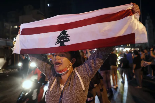 An anti-government protester chants slogans as she holds up a Lebanese flag joining others to block a road during a protest against the political leadership they blame for the economic and financial crisis, in Beirut, Lebanon, Thursday, June 11, 2020. (Photo by Hussein Malla/AP Photo)