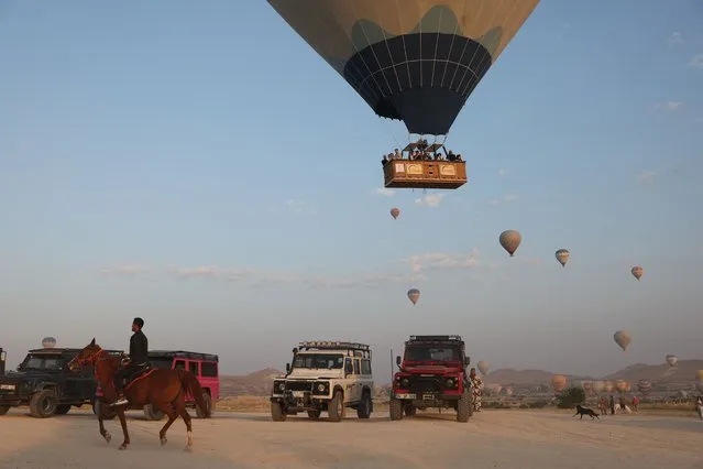 Trucks below await the landing of hot air balloons launched over Goreme Historical National Park, east of Nevesehir (Neapolis) in the province of the same name in central Turkey's historical Cappadocia (Kapadokya) region on August 24, 2022. (Photo by Omar Haj Kadour/AFP Photo)