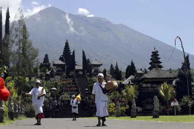 Balinese religious devotees walk as they visit the Besakih temple with Mount Agung volcano in the background which is located only a few kilometers (miles) from the crater in Karangasem, Bali, Indonesia, Monday, October 30, 2017. Indonesia authorities lowered the alert status of Bali's Mount Agung volcano from the highest level on Sunday, following a significant decrease in activity in recent days. (Photo by Firdia Lisnawati/AP Photo)