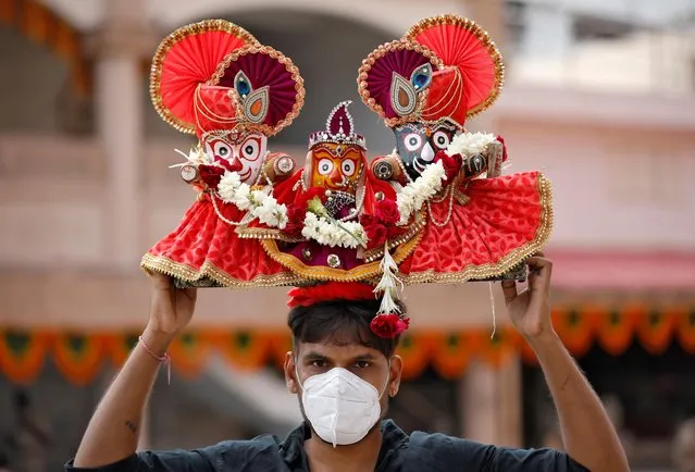 A Hindu devotee, wearing a protective face mask, carries idols of Hindu Lord Jagannath, his sister Subadhra and brother Balabhadra, as he arrives to attend the annual Rath Yatra, or chariot procession, amidst the coronavirus disease (COVID-19) outbreak, in Ahmedabad, India, June 23, 2020. (Photo by Amit Dave/Reuters)