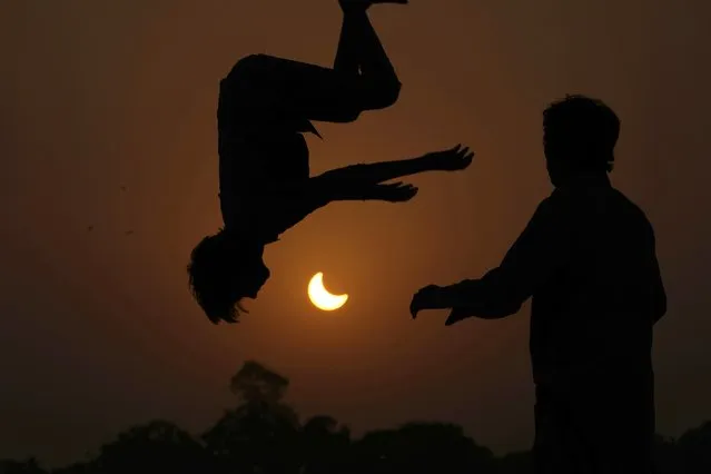 The partial solar eclipse is framed by youngsters jumping on a trampoline in the outskirts of Lahore, Pakistan, Tuesday, October 25, 2022. (Photo by K.M. Chaudary/AP Photo)