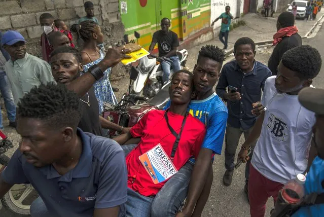 People help a journalist affected by tear gas launched by police during a protest over the death of a journalist Romelo Vilsaint, in Port-au-Prince, Haiti, Sunday, October 30, 2022. (Photo by Ramon Espinosa/AP Photo)