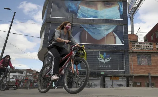 Women wearing protective face masks pedal past on bicycles in Bogota, Colombia, Thursday, July 23, 2020, amid the new coronavirus pandemic. As COVID-19 cases in Colombia continue to climb, the mayor of Bogota has imposed social distancing measures. (Photo by Fernando Vergara/AP Photo)
