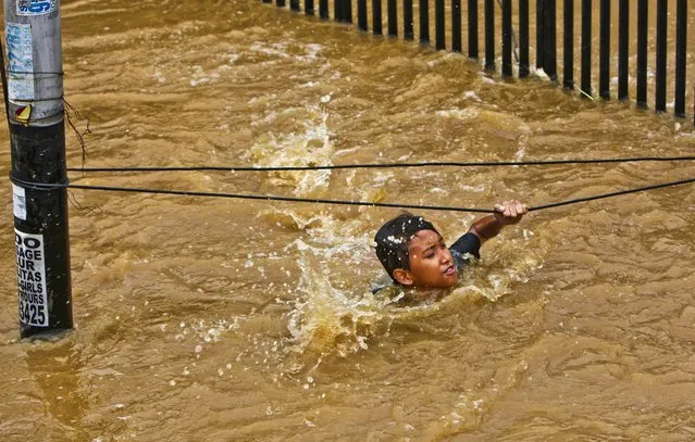 A man grabs wires to keep from being swept away by flood wates in Jakarta, Indonesia, January 18, 2013. Authorities were working to repair a dike that collapsed and flooded  the Indonesian capital. (Photo by Tatan Syuflana/Associated Press)