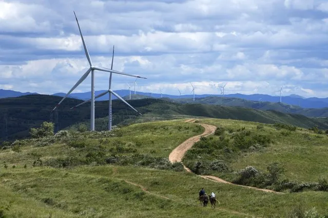 Tourists ride horses near Wind turbines on the grassland in Zhangbei county, in north China's Hebei province on August 15, 2022. The world's two biggest emitters of greenhouse gases are sparring on Twitter over climate policy, with China asking if the U.S. can deliver on the landmark climate legislation signed into law by President Joe Biden this week. (Photo by Andy Wong/AP Photo)