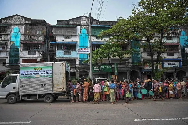 People queue to buy cheap vegetable oil, in Yangon on August 18, 2022. Dozens queued under monsoon drizzle for subsidised cooking oil in Myanmar's commercial hub Yangon, one of the many commodities that have become scarce as economic misery strikes the city, following the last coup and has been further rattled by the junta's attempts to seize scarce foreign exchange and erratic rules governing businesses and imports. (Photo by AFP Photo/Stringer)